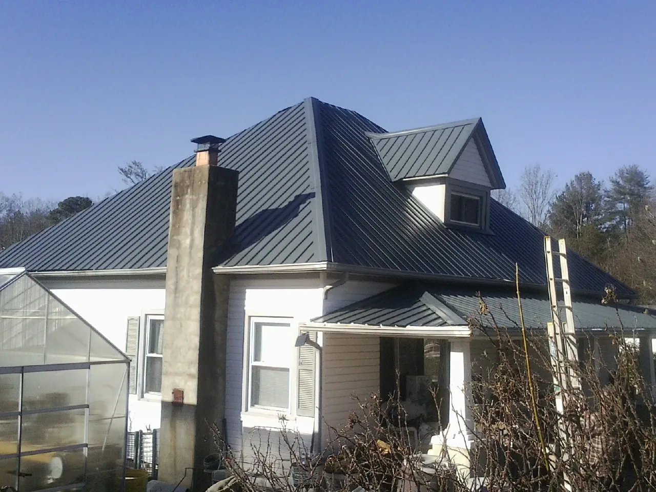 Dark blue standing seam metal roof on a white farmhouse with dormer — Slate & Tile Roof Repair by Roofing Brothers in Eastlake