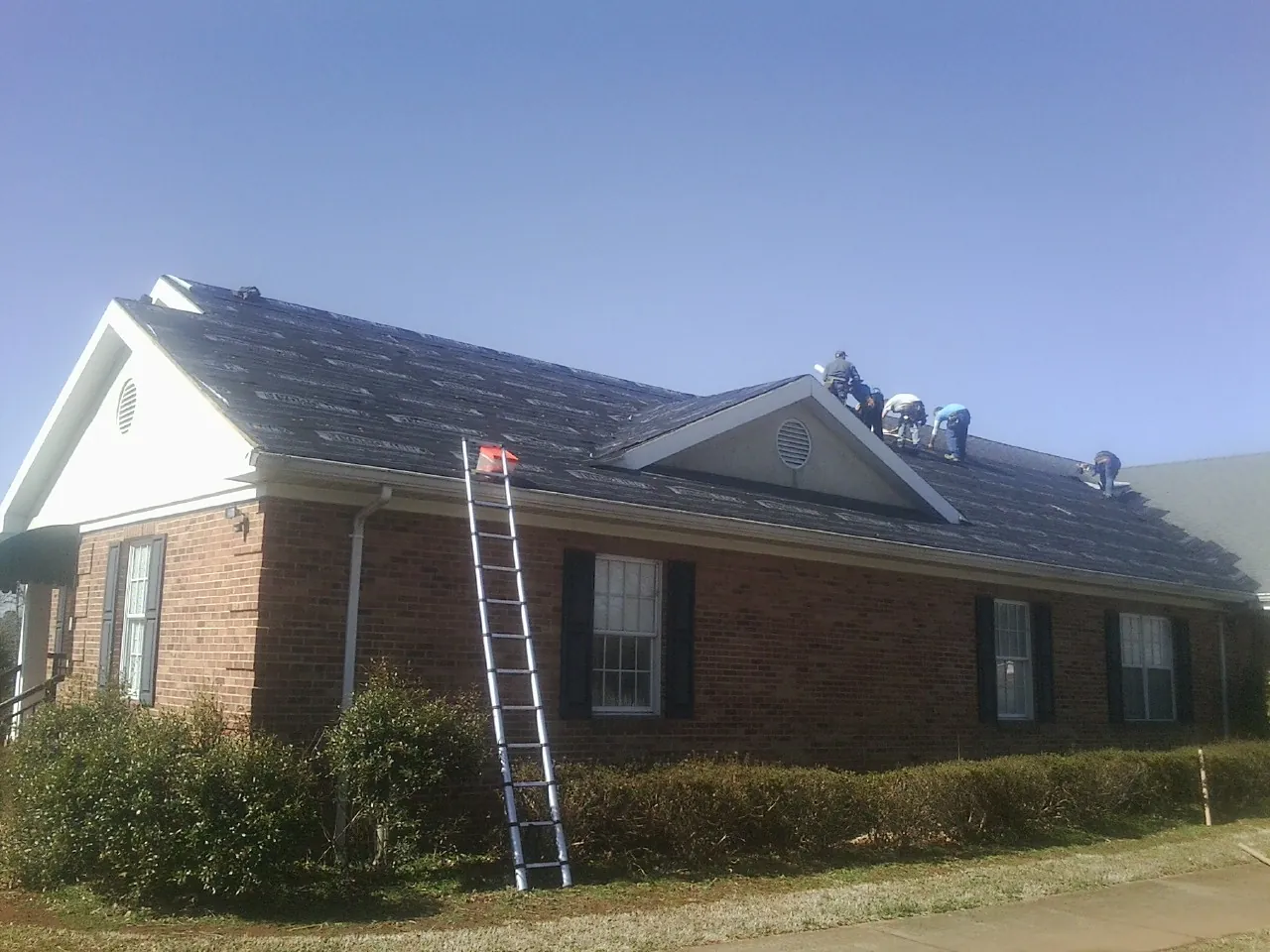 Crew tearing shingles off a brick ranch roof with a ladder set — Metal Roof Repair work by our crew in Eastlake