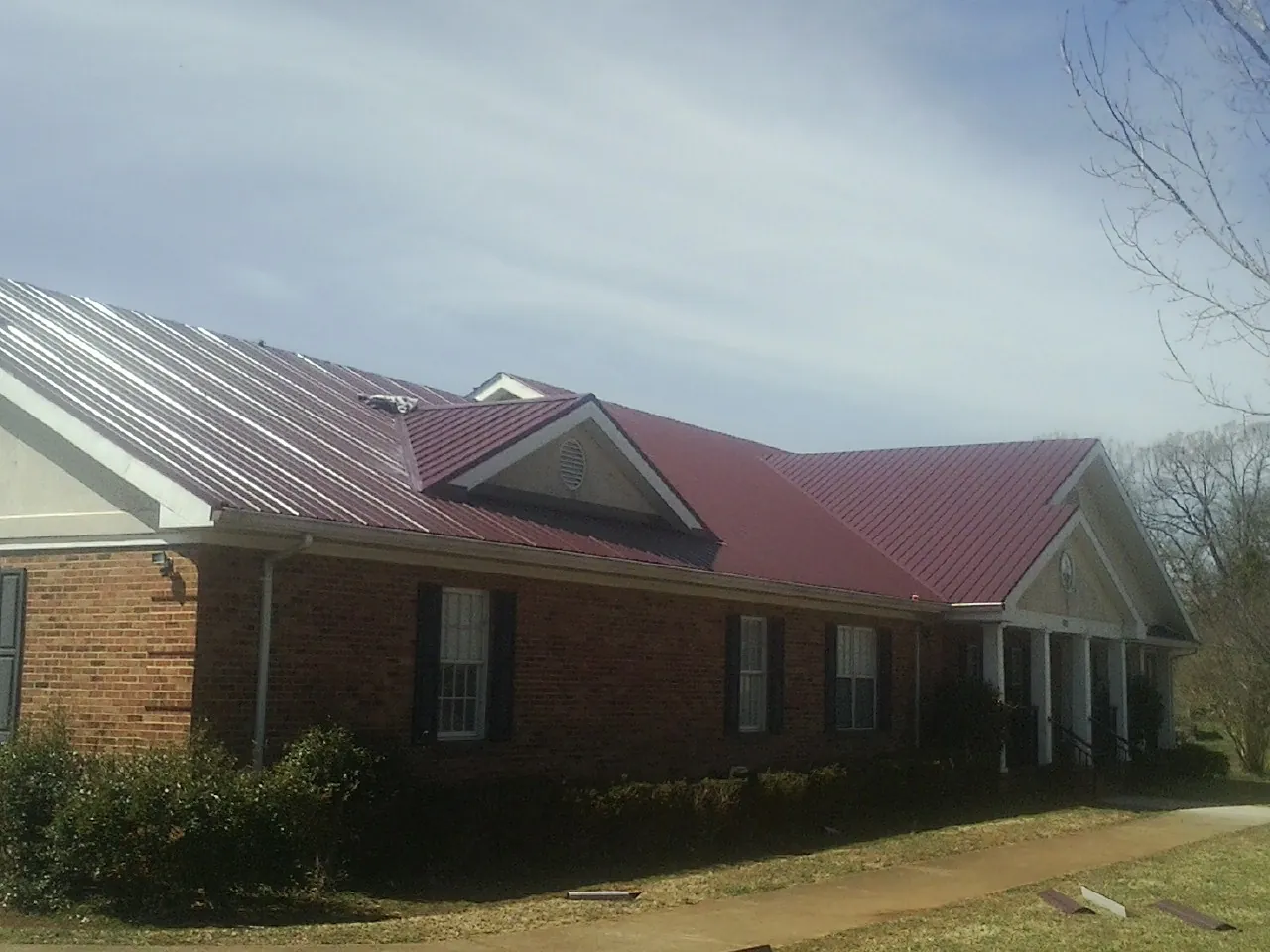 Red metal roof with gabled entries on a long brick building, from a Hail Damage Roof Repair job in Eastlake