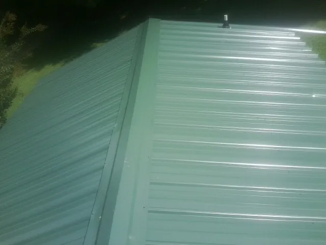 New green metal panels meeting at the ridge of a roof — Flat Roof Repair work by our crew in Eastlake