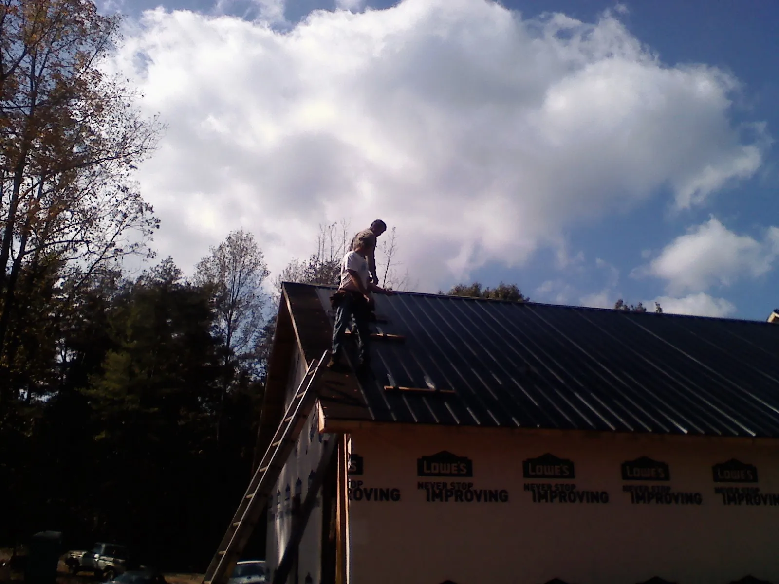 Roofer fastening dark metal panels high against a cloudy sky, from a Roof Inspection job in Eastlake