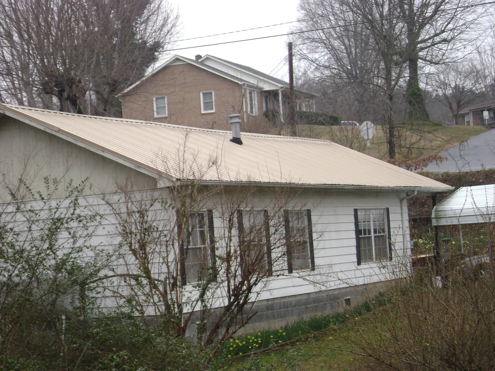 Tan metal roof on a white sided house set into a hillside — Commercial Roofing by Roofing Brothers in Eastlake